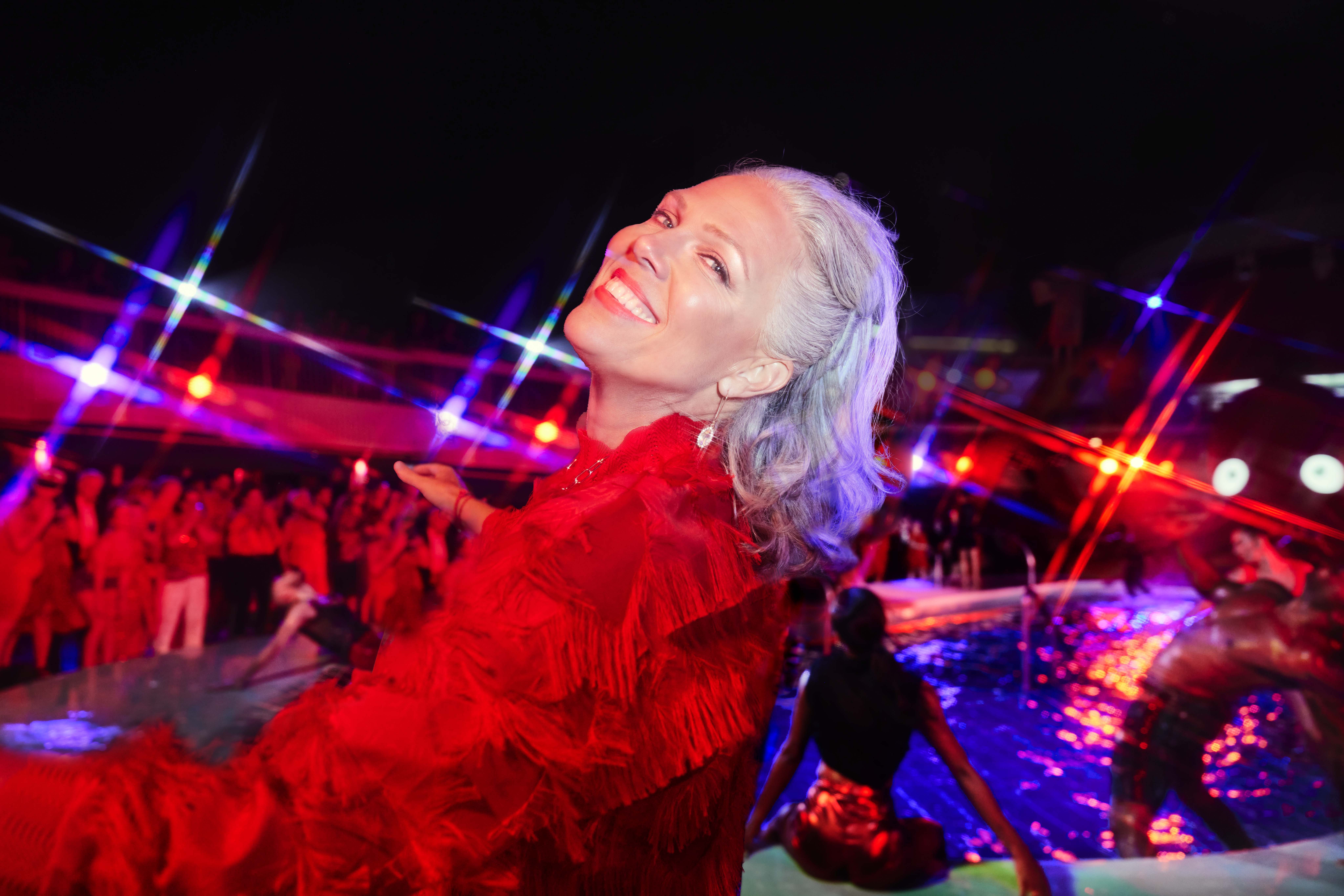 A woman smiles at the camera during Scarlet Night. There's a party behind her and everyone is wearing red. 

Alberto Oviedo, Lifestyle, Now We're Voyaging
Now We're Voyaging Campaign
Photographer: Alberto Oviedo
Studio: Christian Schrader, Kathy Boos
Brand: Billy Bohan