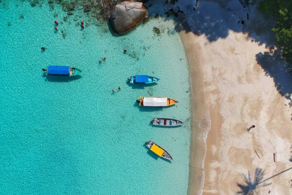 Aerial view of a Caribbean beach with small boats anchored — typical port-day scene on a Caribbean gay cruise